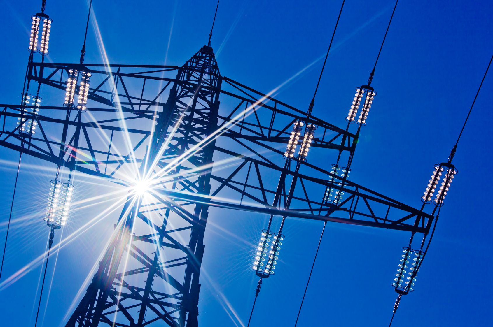 Ein Hochspannungsmasten für Strom vor blauem Himmel und Sonnenstrahlen