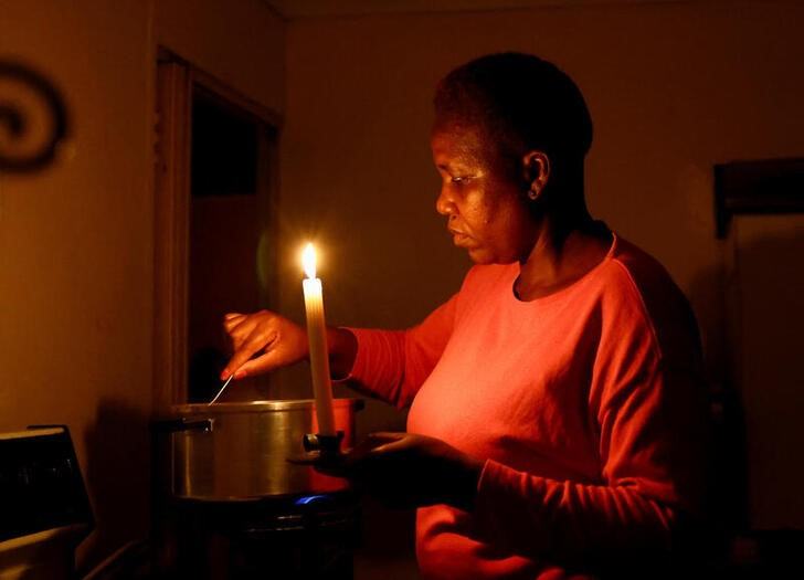 Maria Modiba cooks by a candlelight during one of the frequent power outages from South African utility Eskom, caused by its aging coal-fired plants, in Soweto, South Africa November 11, 2022. REUTERS/Siphiwe Sibeko